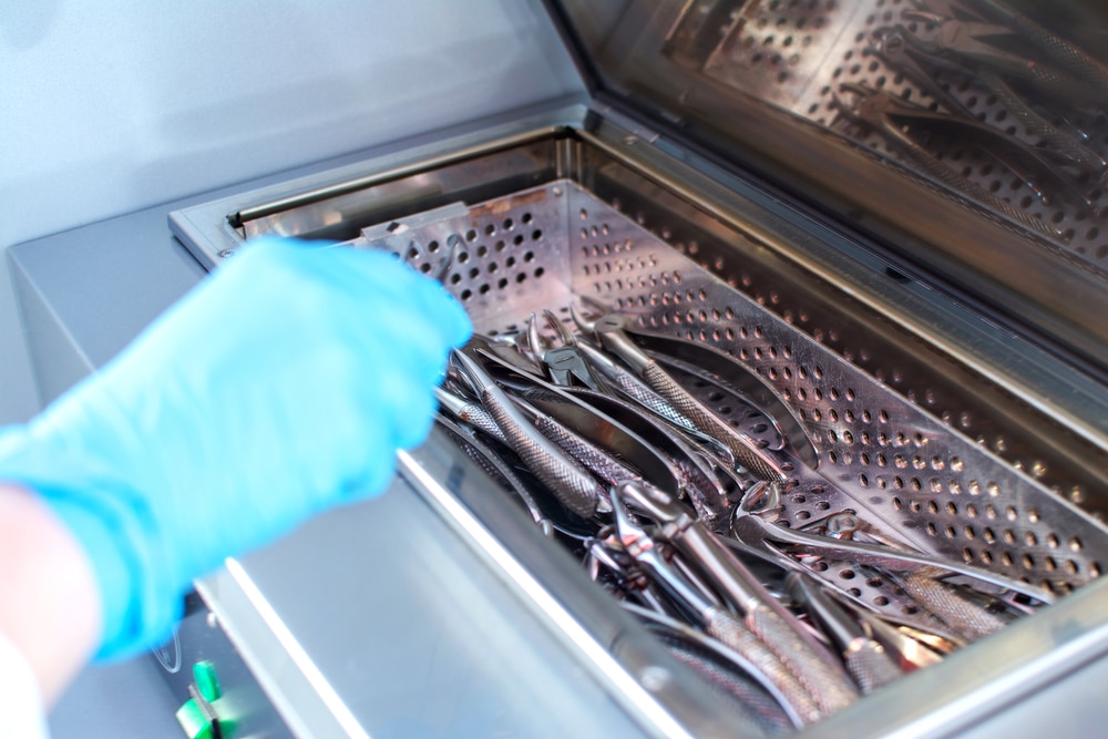 Close up of dentist's hands taking out sterilizing medical instruments from autoclave.